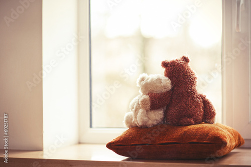 Obraz na plátně Two embracing teddy bear toys sitting on window-sill