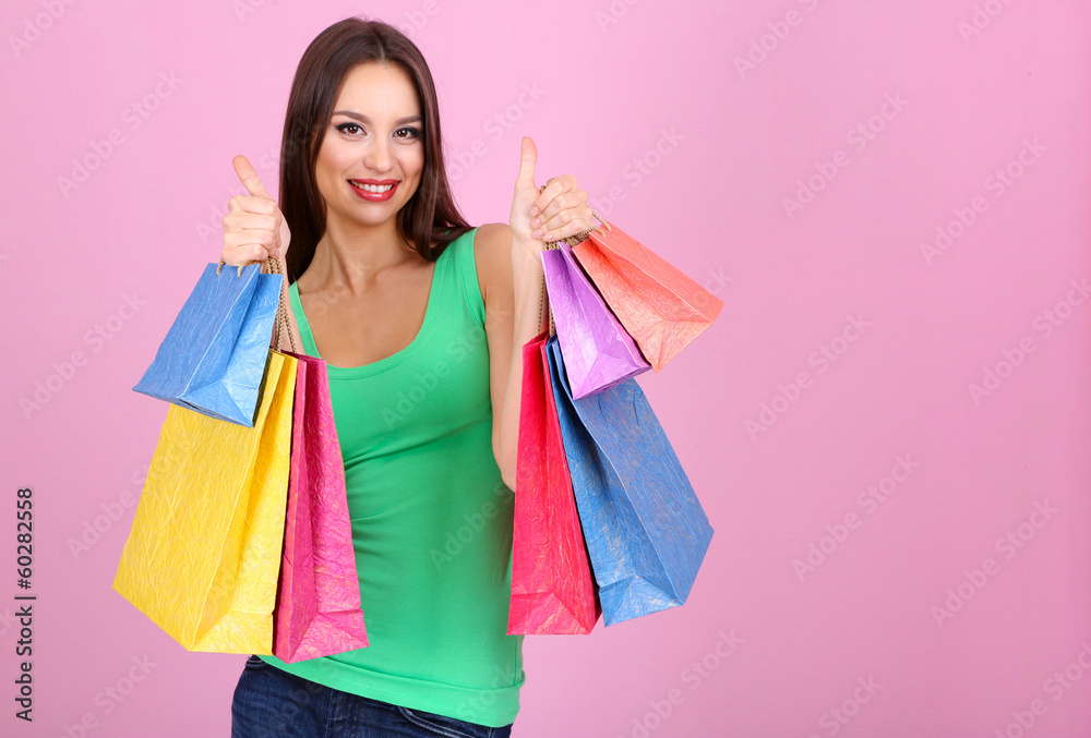 Beautiful young woman holding shopping bags on pink background