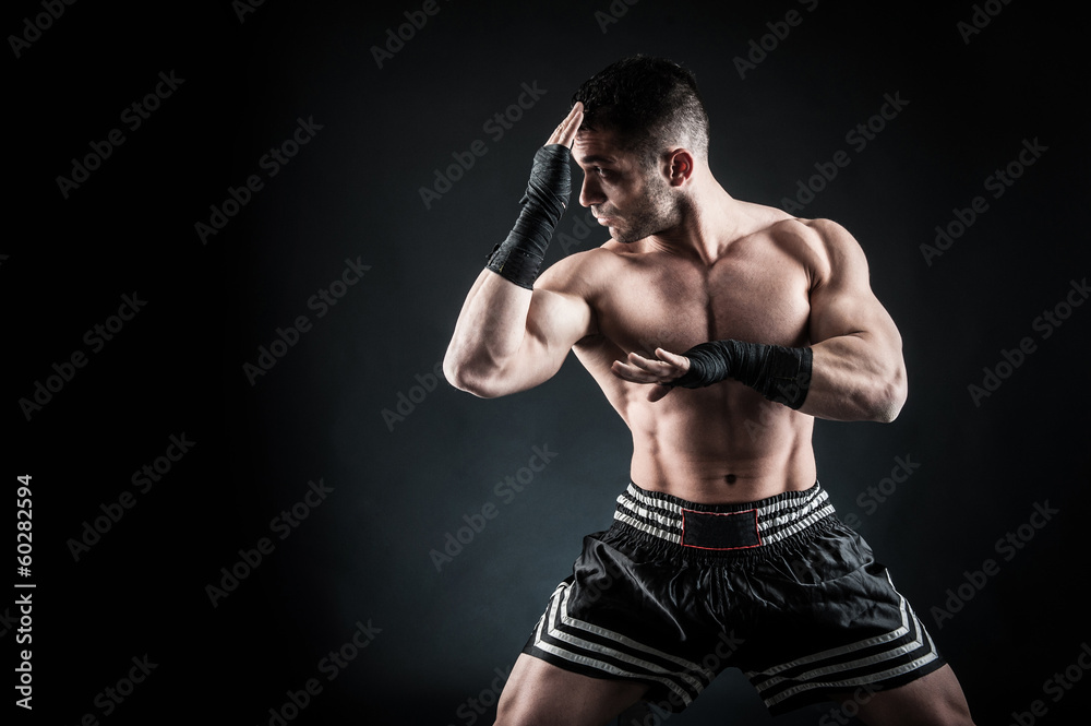 Sportsman kick boxer intense portrait against black background.