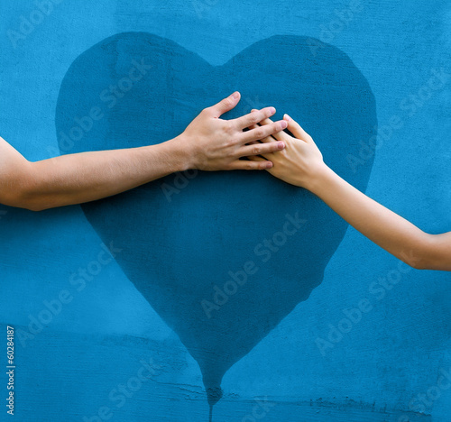 Male and female hands touching painted heart on concrete wall photo