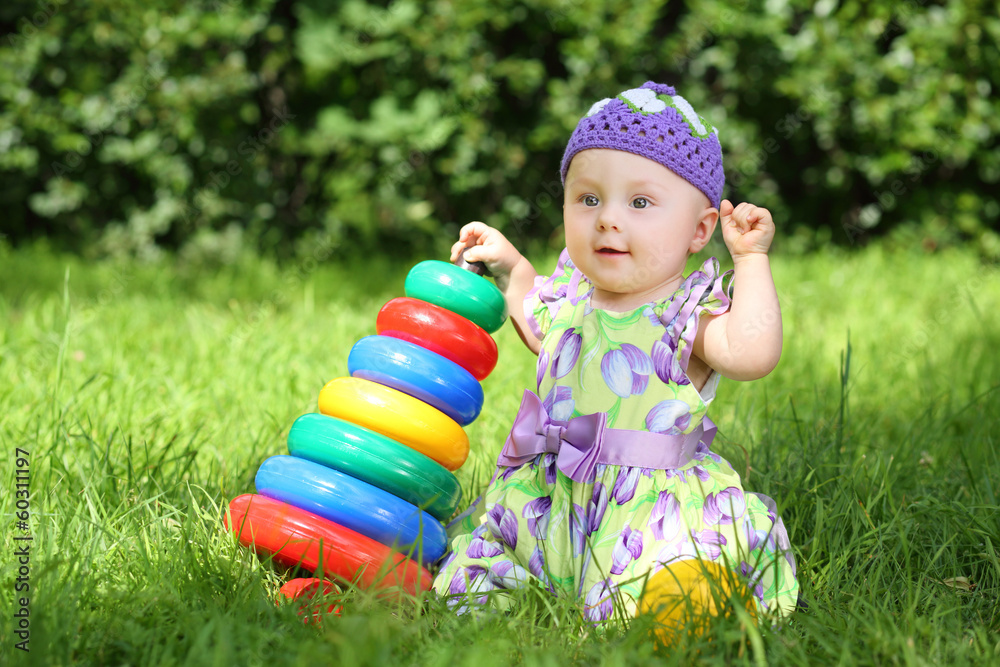Smiling little girl playing with colorful pyramid on the grass Smiling little girl playing with colorful pyramid on the grass