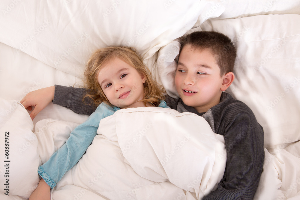 Protective young boy in bed with his little sister