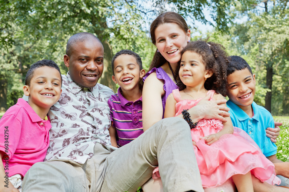 Interracial laughing family of six sits on grass on lawn Interracial laughing family of six sits on grass on lawn