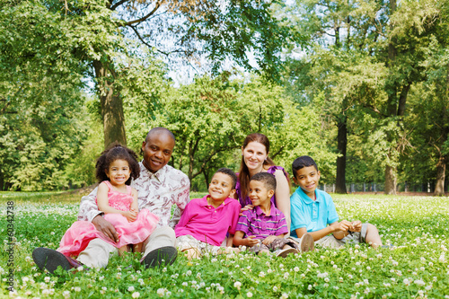 Interracial family of six sits on grass on lawn in park