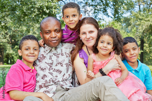 Big interracial family of six sits tight embraced in grass