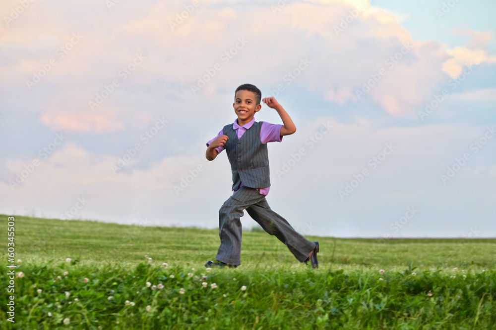 Cheerful little boy runs on grassy meadow