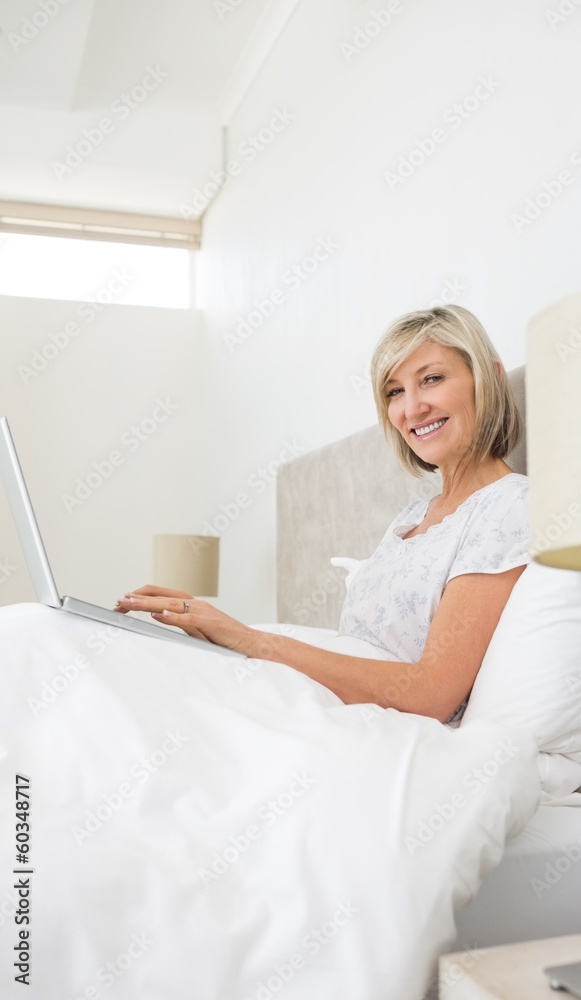 Smiling mature woman using laptop in bed Smiling mature woman using laptop in bed