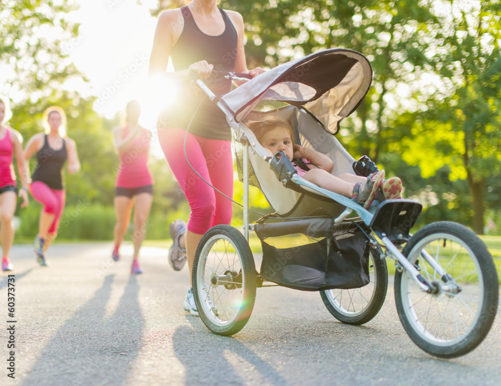 Woman pushing her toddler while running in nature with friends - obrazy, fototapety, plakaty 