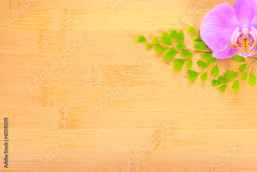 lilac orchid and leaves of fern on bamboo wooden background