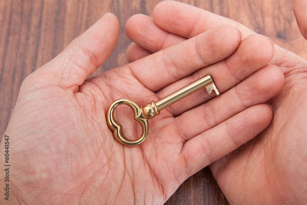 Person's Hand On Wooden Table Holding Golden Key