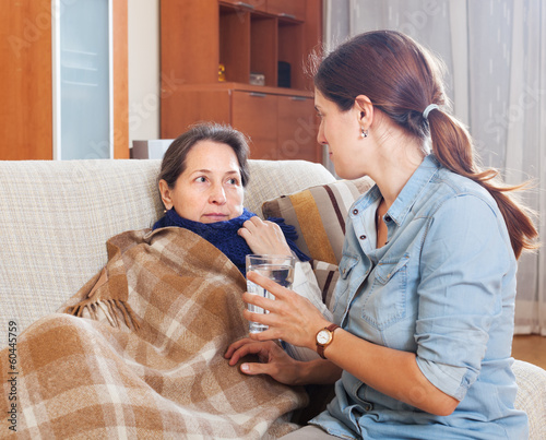  daughter giving the glass of water to sick mature mother