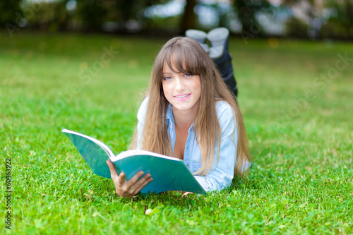 Young beautiful female student reading a book on the grass