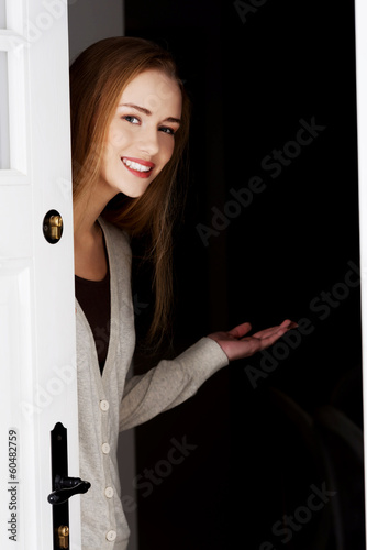 Beautiful woman is opening door and inviting to come in.