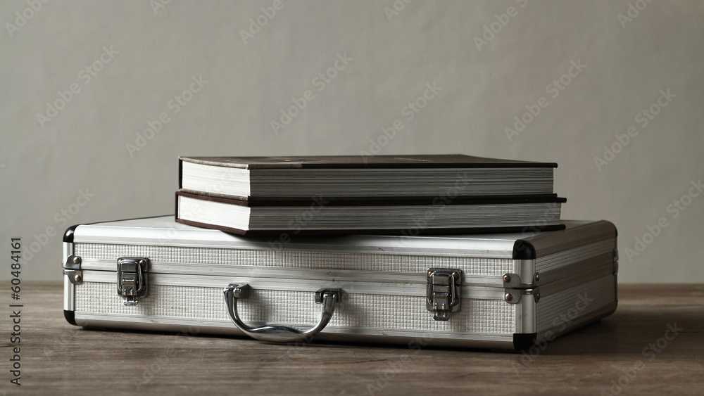 Books over aluminum suitcase on wooden table Books over aluminum suitcase on wooden table