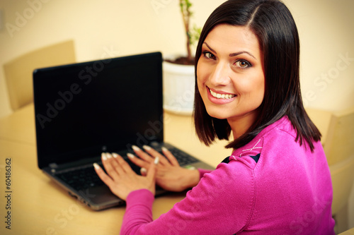 Middle-aged smiling woman using laptop and looking on the camera