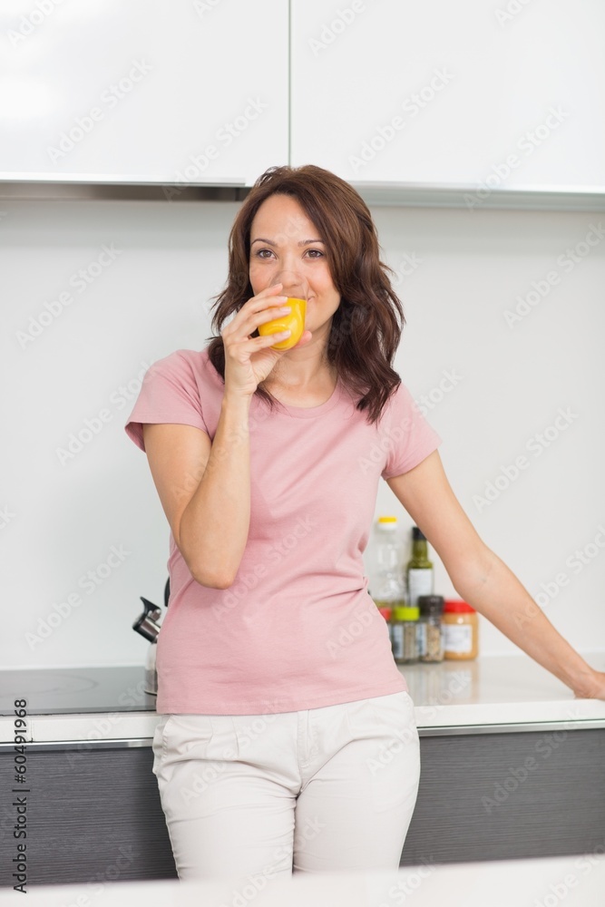 Smiling woman drinking orange juice in kitchen Smiling woman drinking orange juice in kitchen
