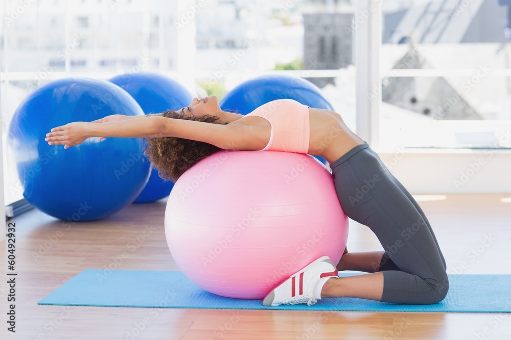 Naklejka premium Side view of a fit woman exercising on fitness ball at gym