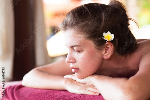 beautiful young woman with flower in hair lying in spa