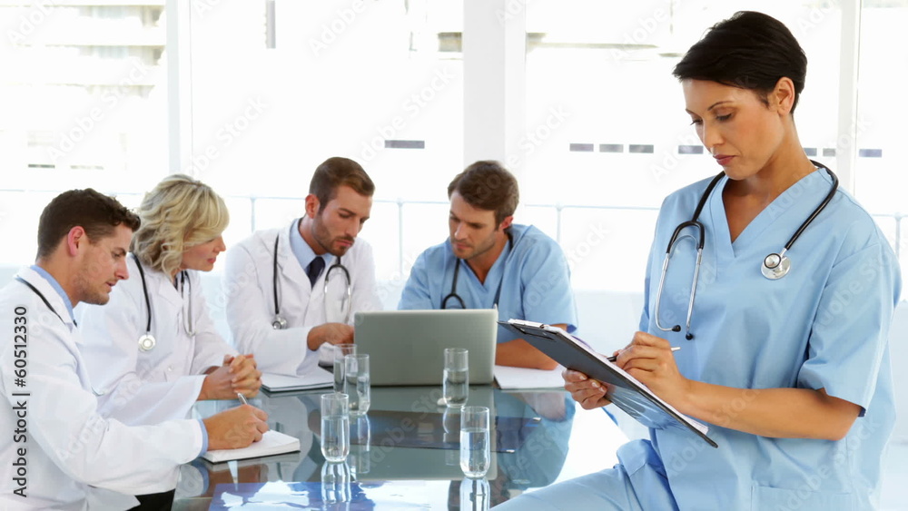 Thoughtful surgeon writing on clipboard with staff talking Thoughtful surgeon writing on clipboard with staff talking
