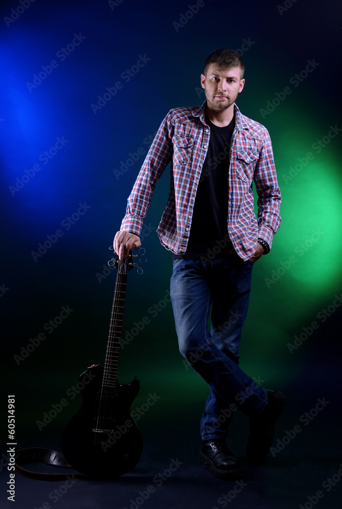Fototapeta premium Young musician with guitar on dark color background