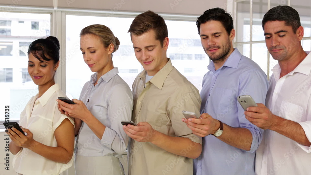 Content businesspeople text messaging while standing in a row
