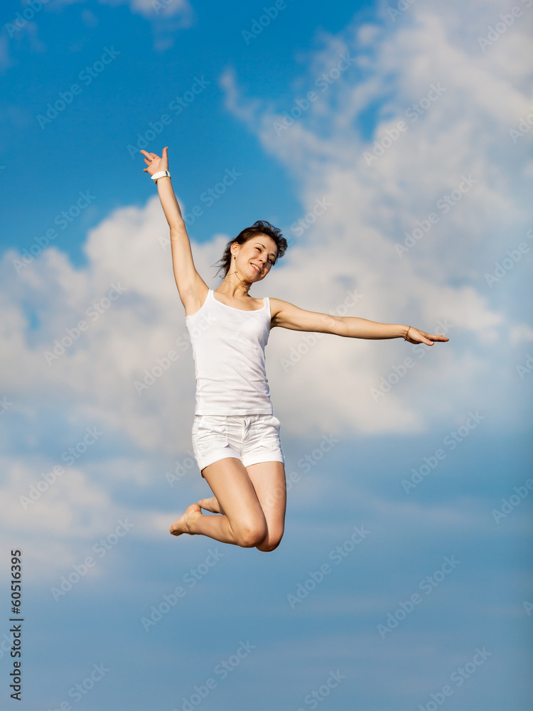 Girl in white hopping with arm raised on background of sky Girl in white hopping with arm raised on background of sky