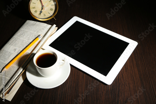 Tablet, newspaper, cup of coffee and alarm clock on wooden