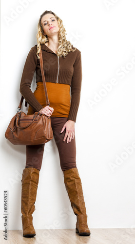 standing woman wearing brown clothes and boots with a handbag