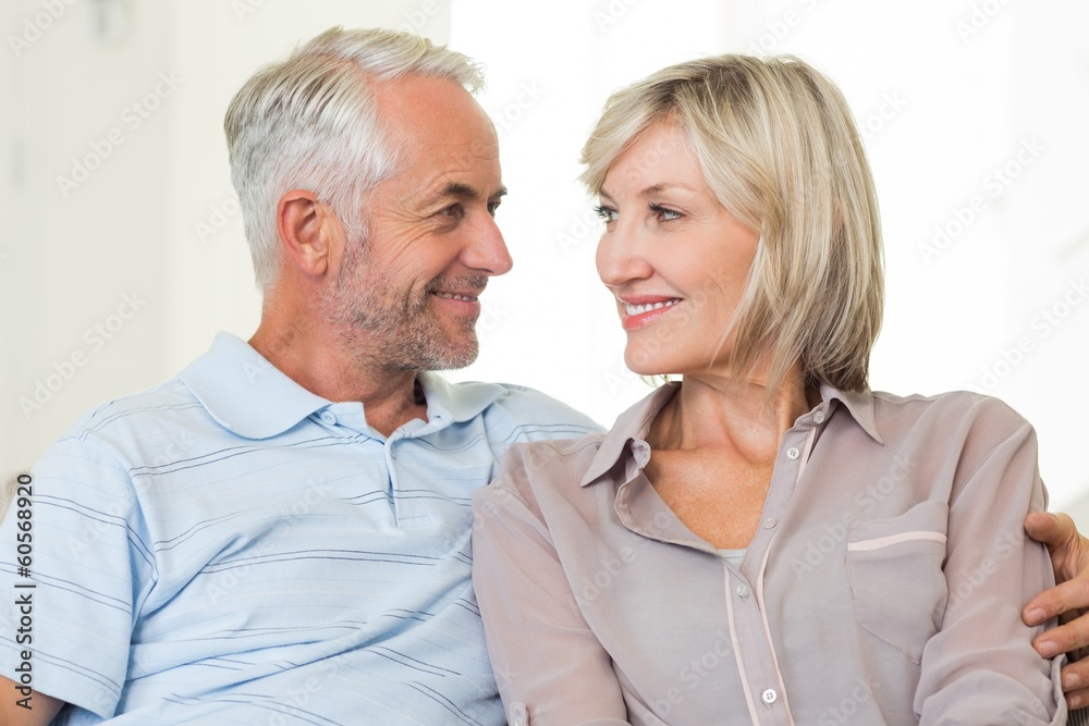 Smiling mature couple sitting on sofa with arm around Smiling mature couple sitting on sofa with arm around