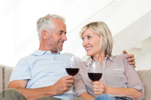 Smiling mature couple with wine glasses sitting on sofa