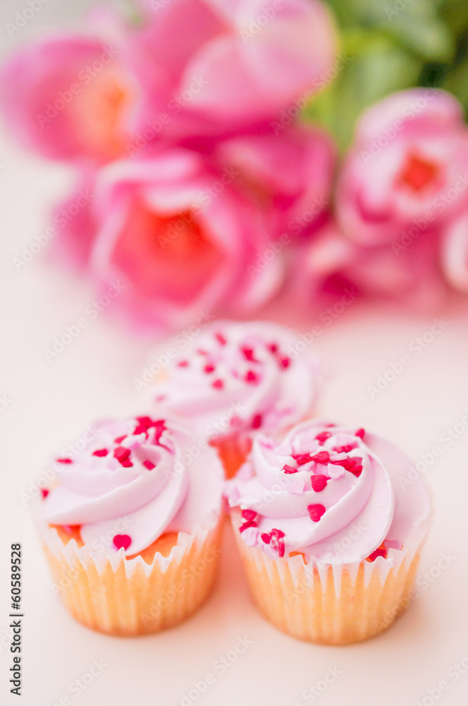 Cupcakes with pink cream,heart sprinkles and tulips on white tab