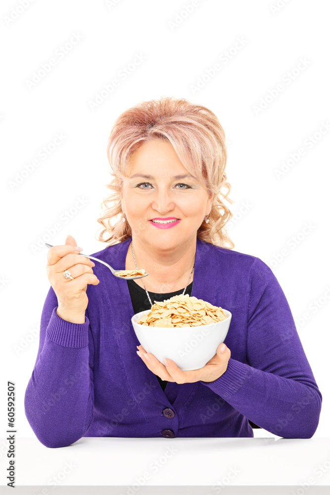 Mature lady eating cereal from a bowl seated on table Mature lady eating cereal from a bowl seated on table