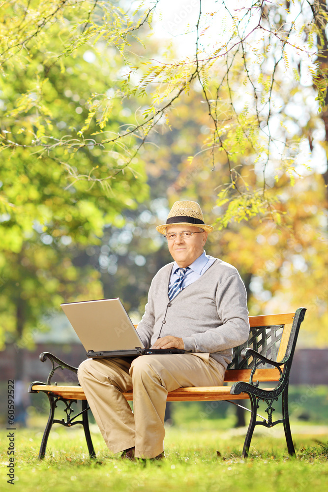 Senior gentleman working on laptop seated on bench in park Senior gentleman working on laptop seated on bench in park