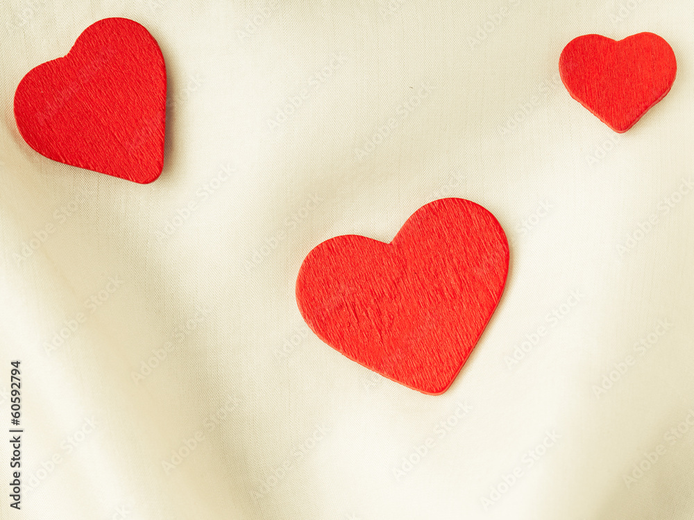 Obraz premium Red wooden decorative hearts on white silk background.