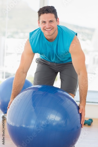 Smiling man exercising with fitness ball at gym