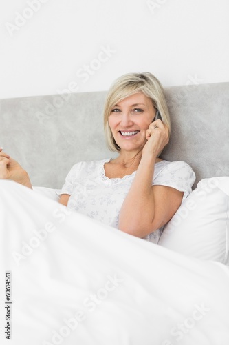 Smiling woman using mobile phone in bed