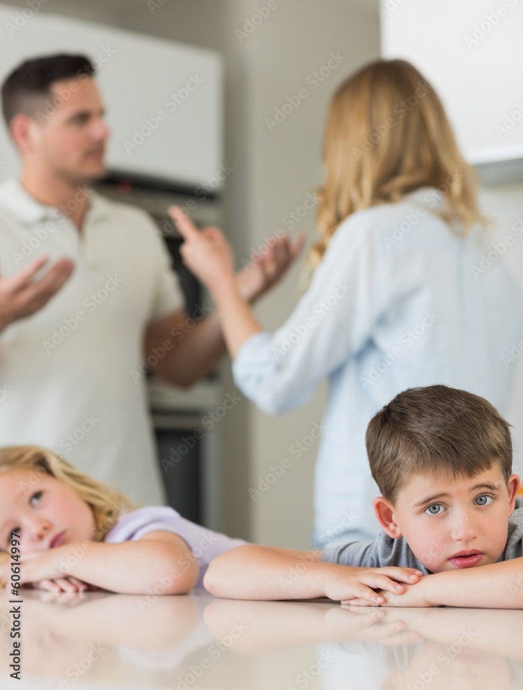 Sad children leaning on table while parents arguing Sad children leaning on table while parents arguing