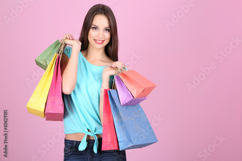 Beautiful young woman holding shopping bags on pink background