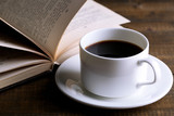 Cup of hot coffee with book on wooden background