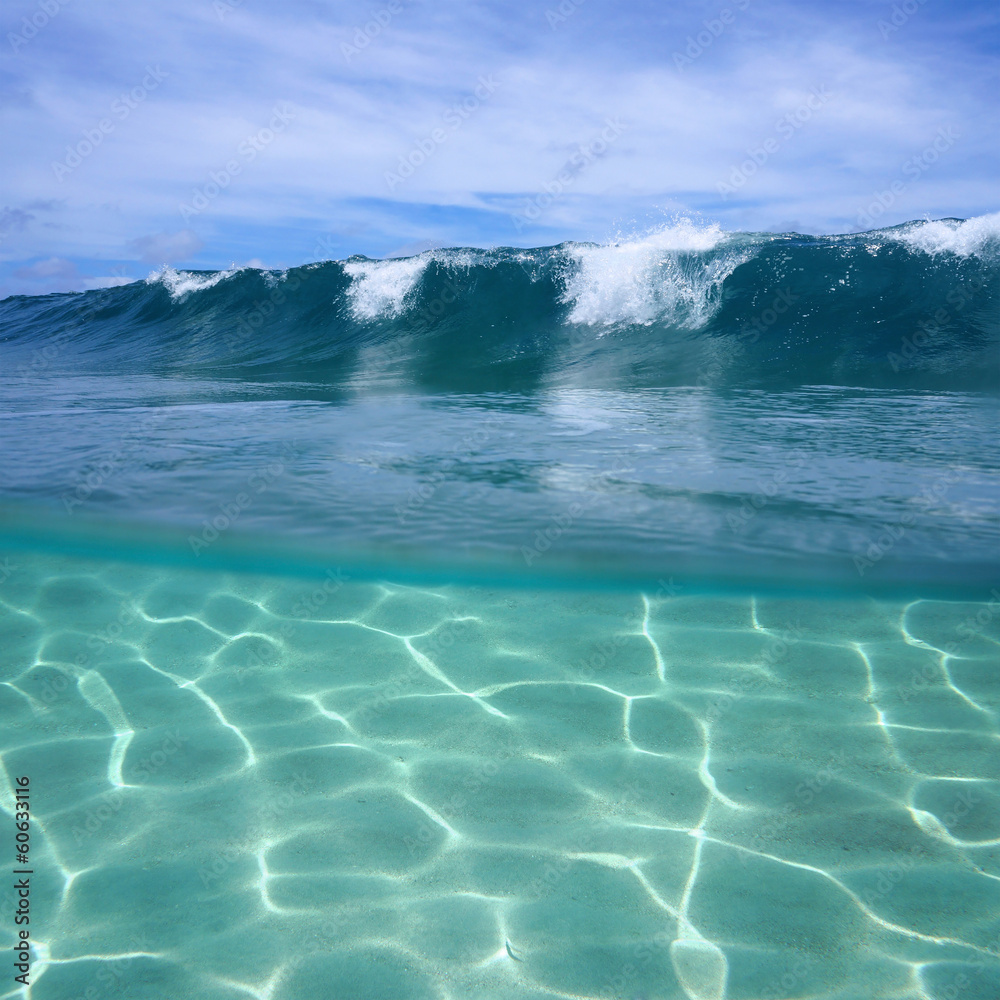 Split view of ocean wave breaking and sandy seabed underwater