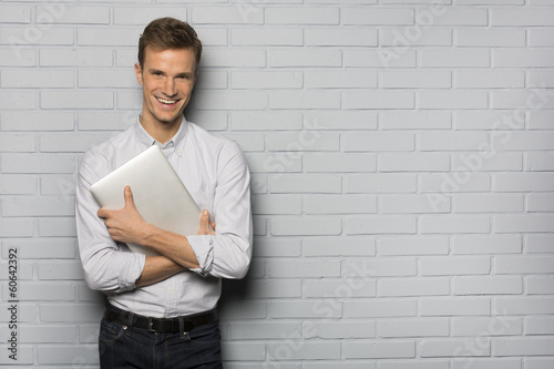 Handsome Cheerful man holding a laptop, isolated over a wall