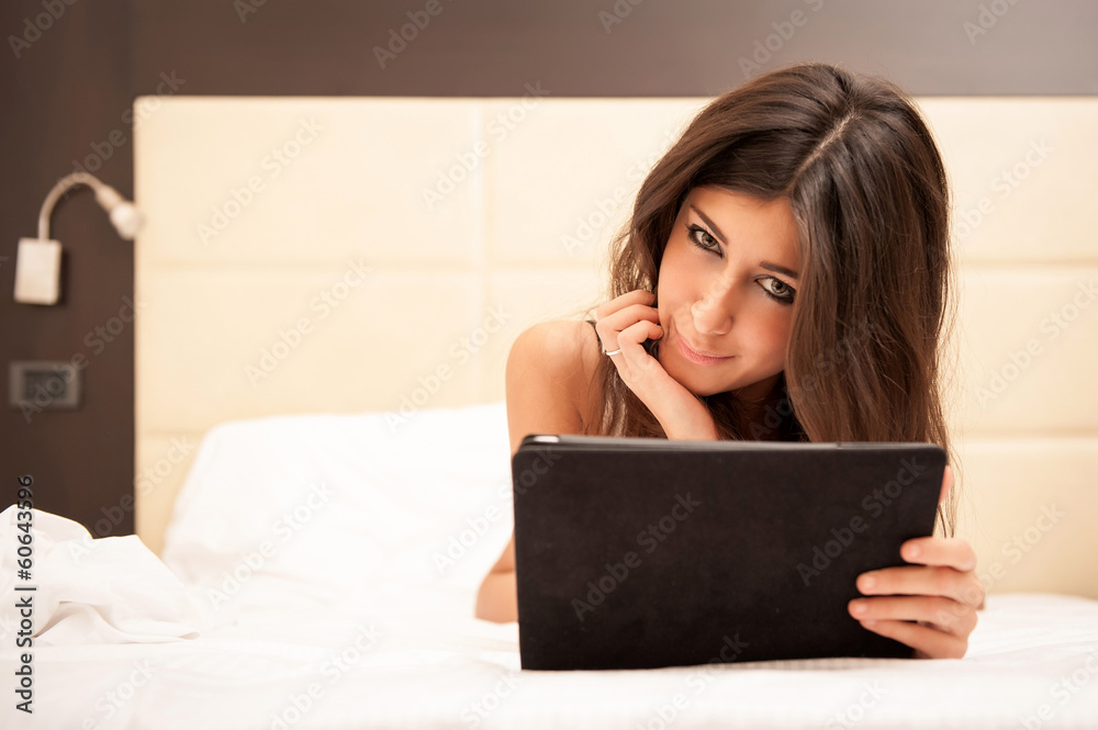 Young woman relaxing on bed while using tablet in hotel room. Young woman relaxing on bed while using tablet in hotel room.