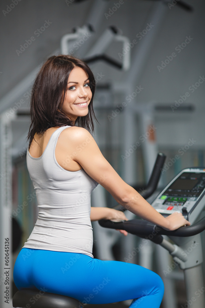 Image of young female training on simulator in gym Image of young female training on simulator in gym