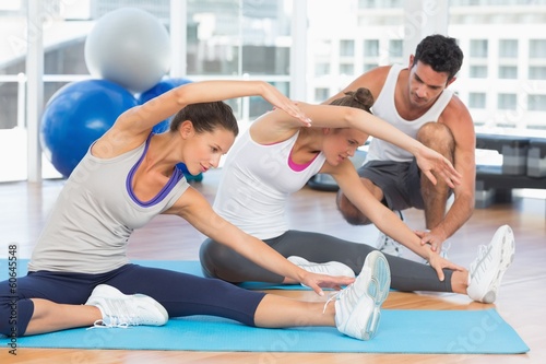 Women doing stretching exercises as trainer helps one