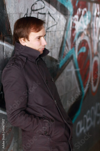 Young man leans back on wall with graffiti and looks aside