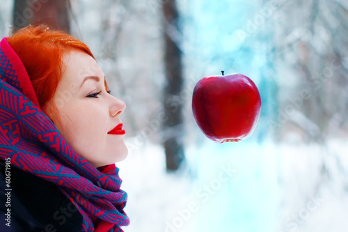 Smiling girl looks at hanging in air big red apple outdoor