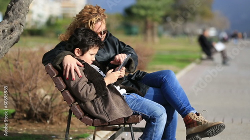 mother and son sitting bank and using tablet computer