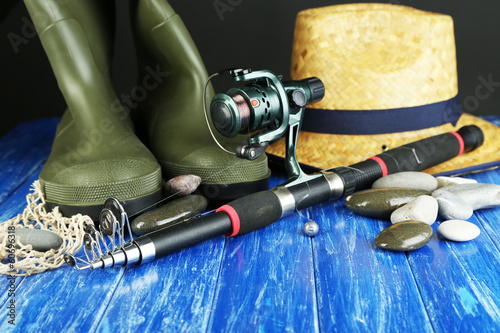 Fishing rod, gumboots and hat on wooden table close-up