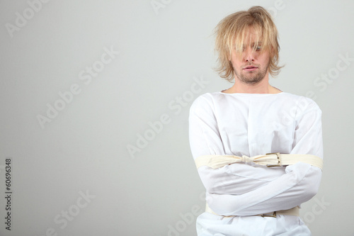 Slika na platnu Mentally ill man in strait-jacket on gray background