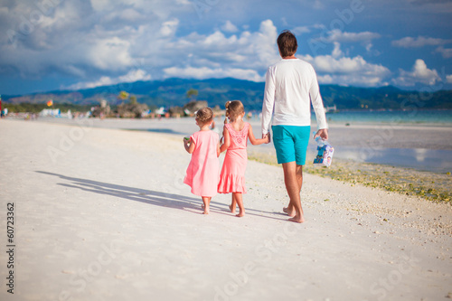 Back view of father and two girls walking on tropical white